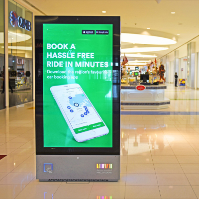 A large digital screen displaying an advertisement for a ride share service in an urban setting.